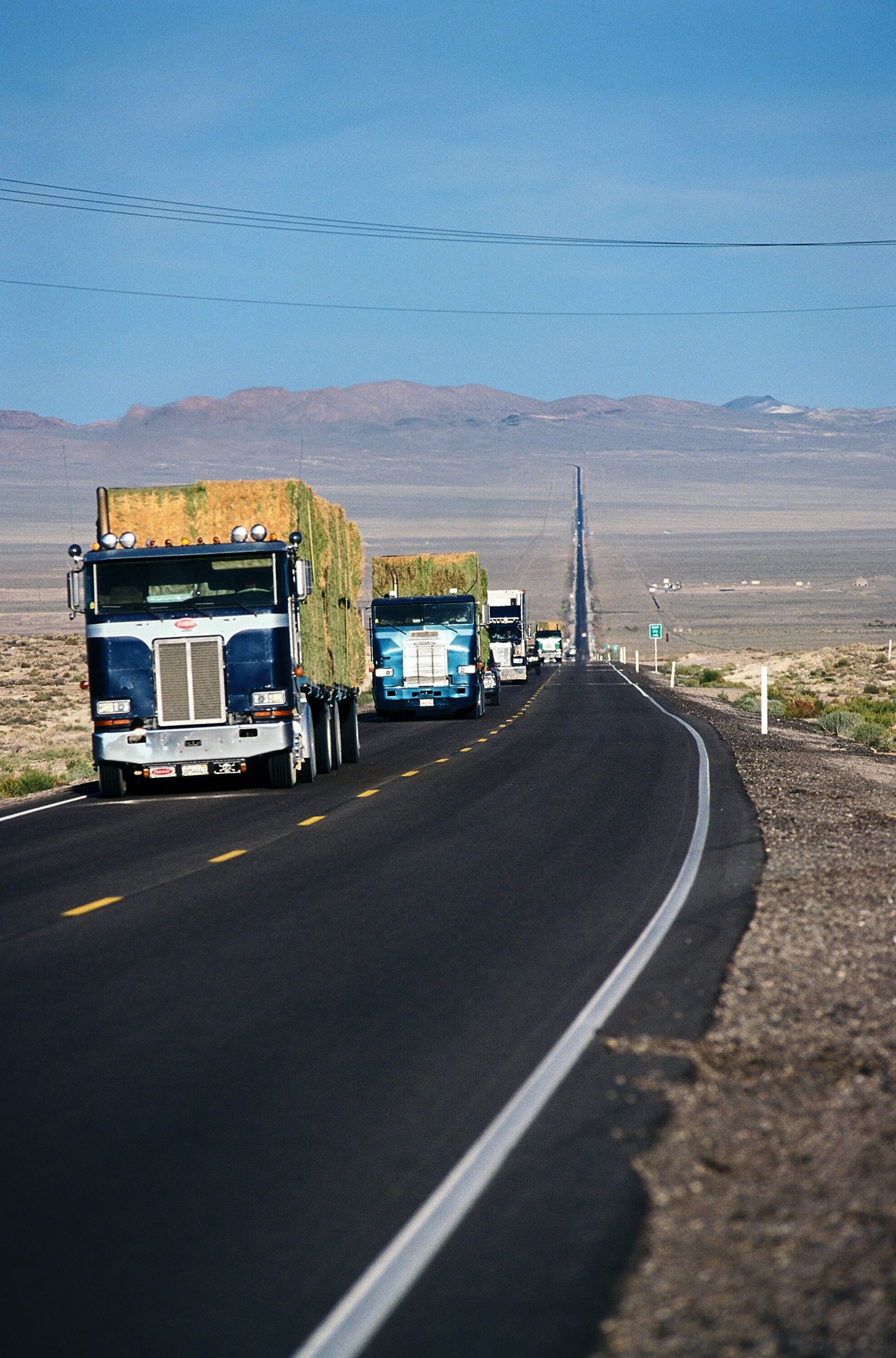 Loaded tractor-trailers running a long two-lane highway across open country